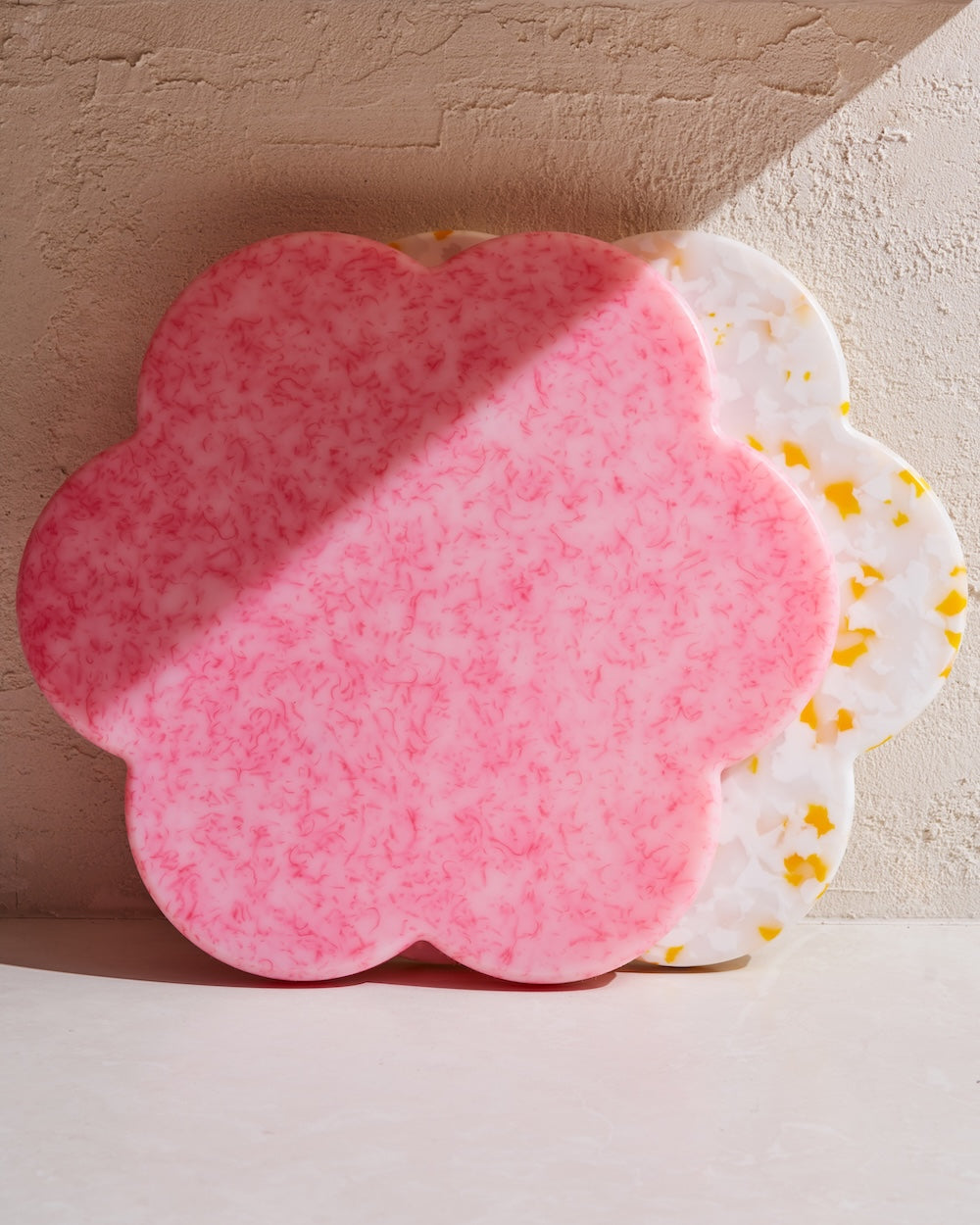 Flower-shaped recycled chopping boards in pink and white with colorful flecks, stacked on a counter
