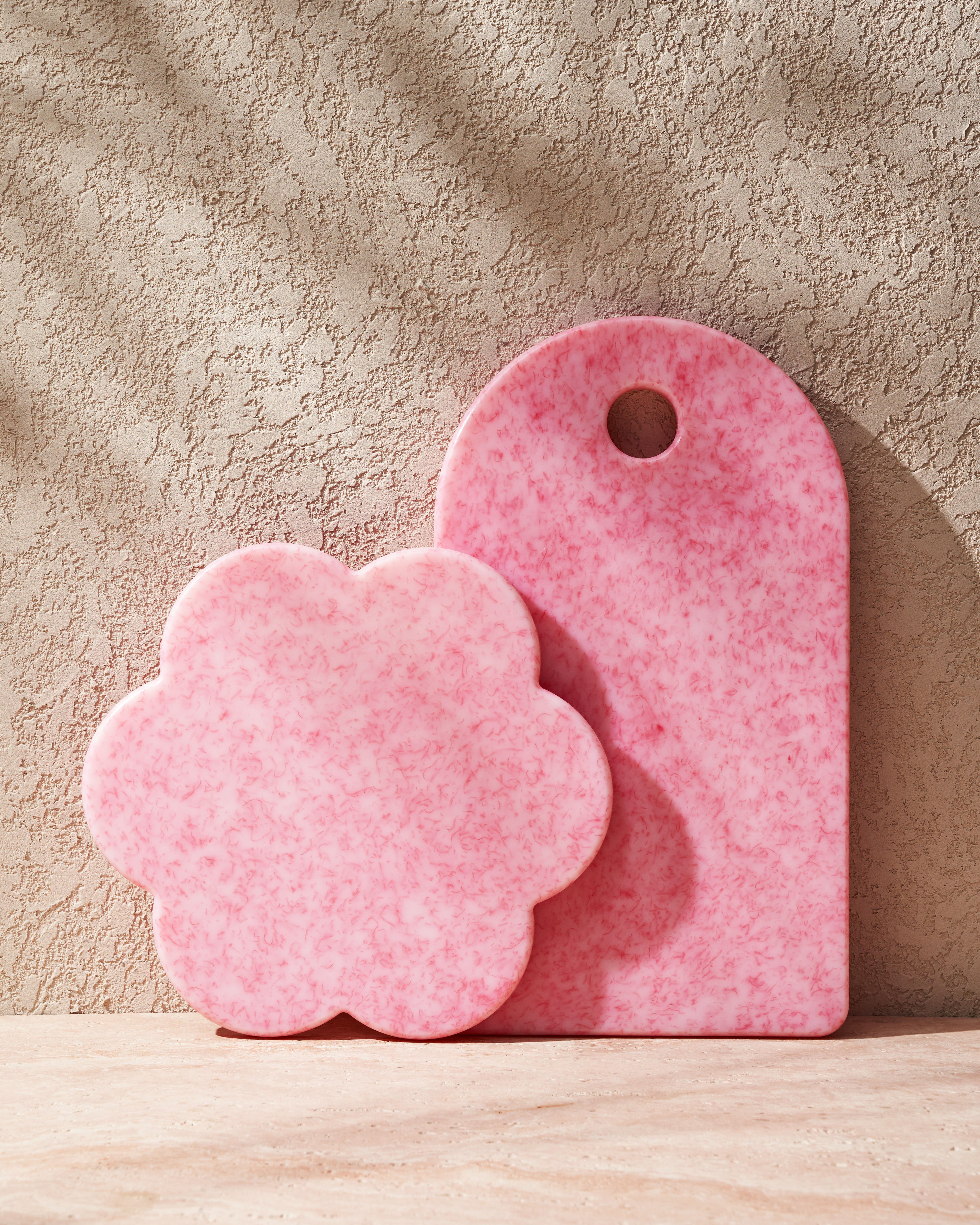 Pink recycled chopping boards, one flower-shaped and one rectangular, on a textured surface