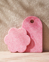 Pink recycled chopping boards, one flower-shaped and one rectangular, on a textured surface