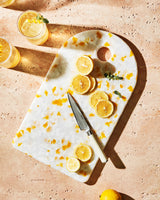 Recycled resin chopping board with yellow accents, sliced lemons, and knife on stone countertop